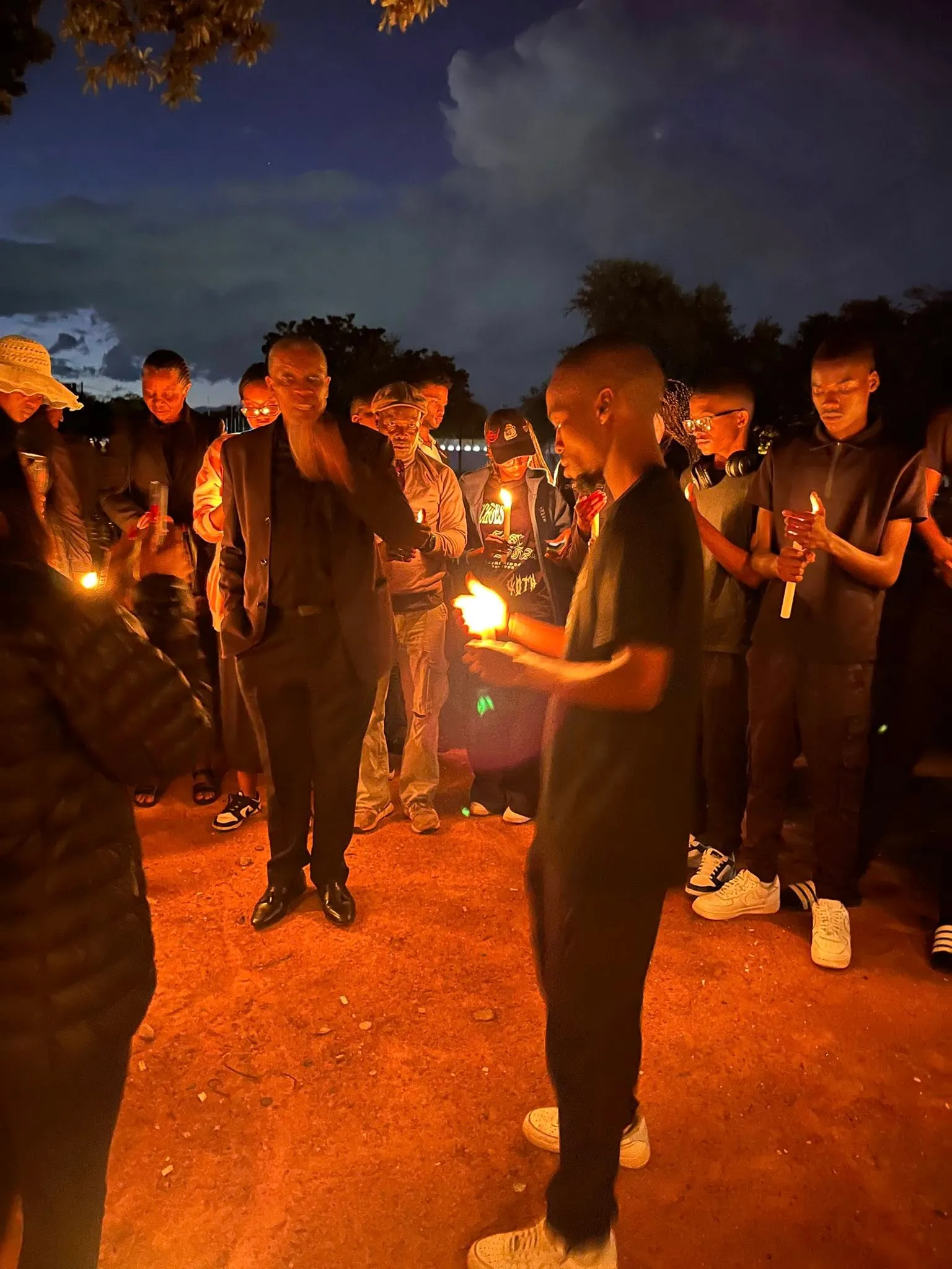 A young man cups a candle flame at a Re A Bua candlelight vigil