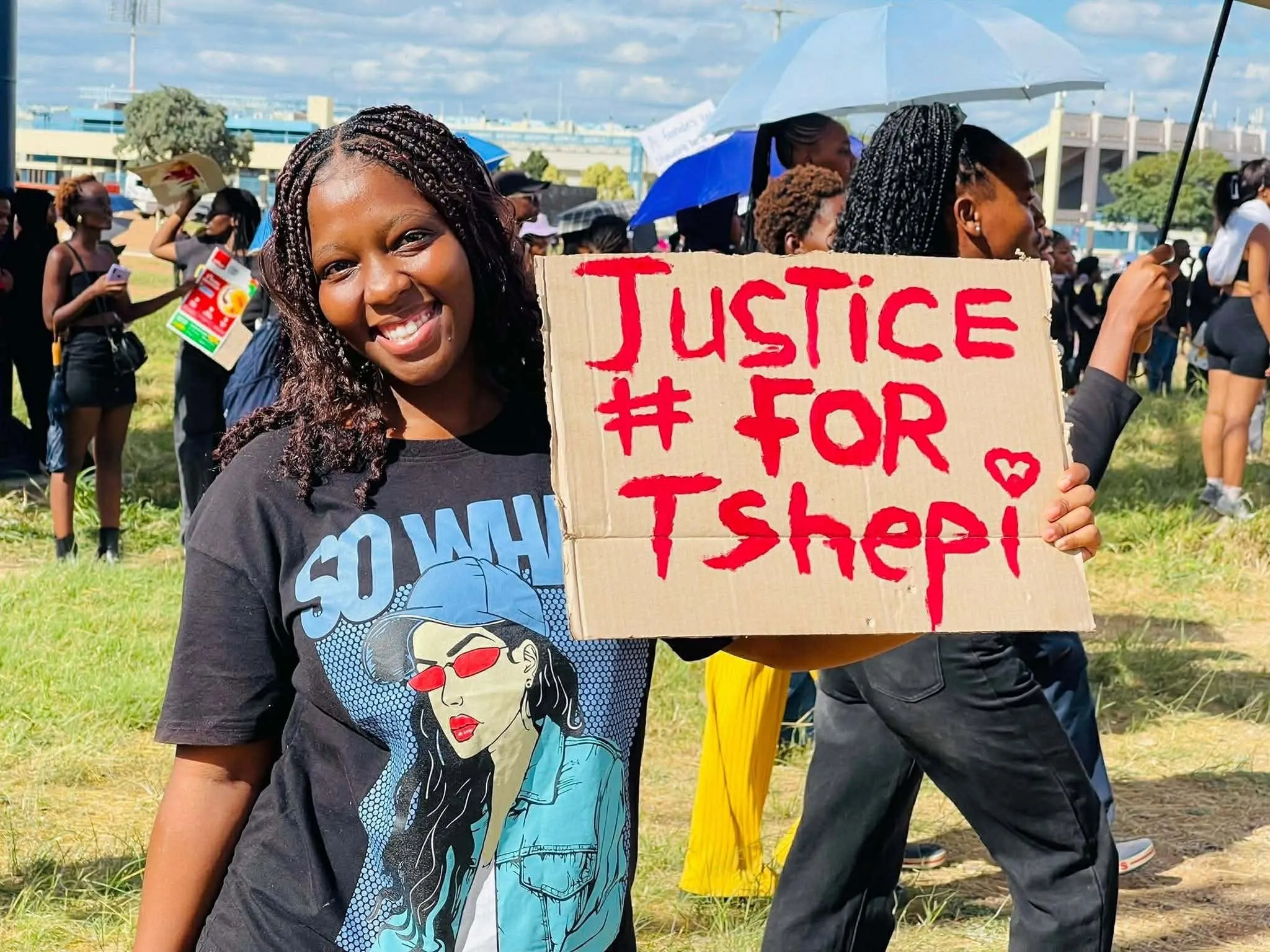 A young woman at the march holds a hand-painted 'Justice for Tshepi' sign
